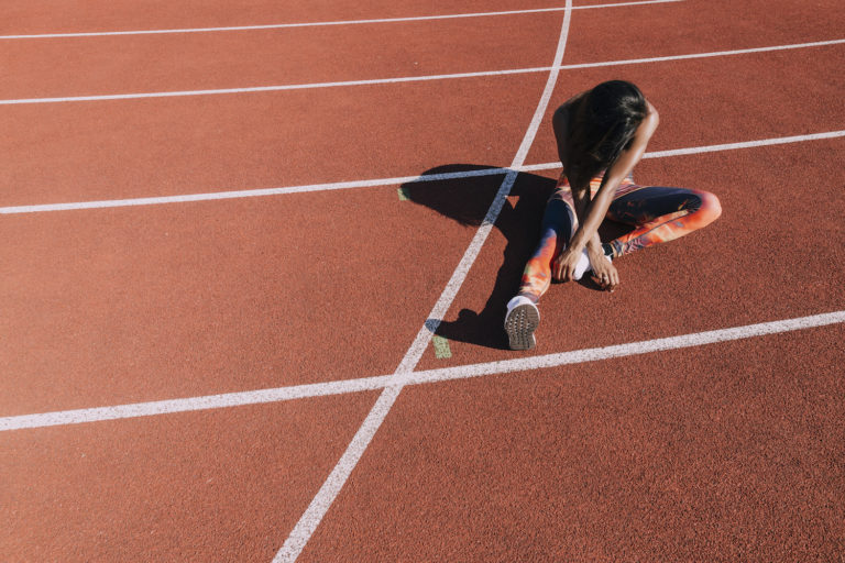 A runner stretches while seated on a track