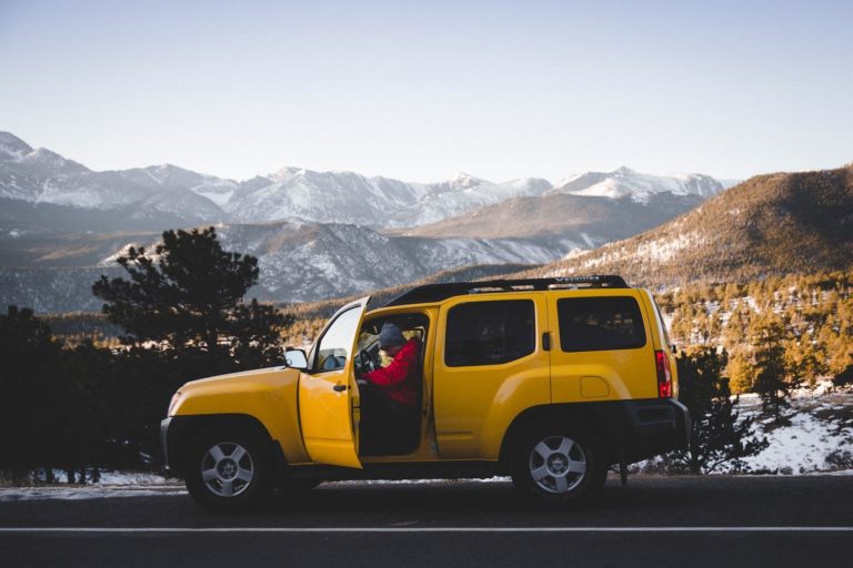 A man steps out of a yellow SUV on a mountain road