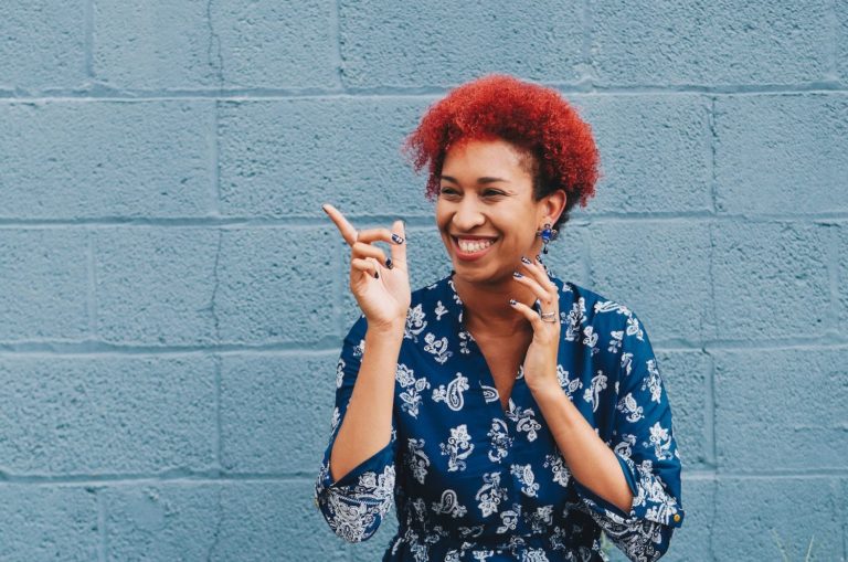 Person of color smiling in front of a wall