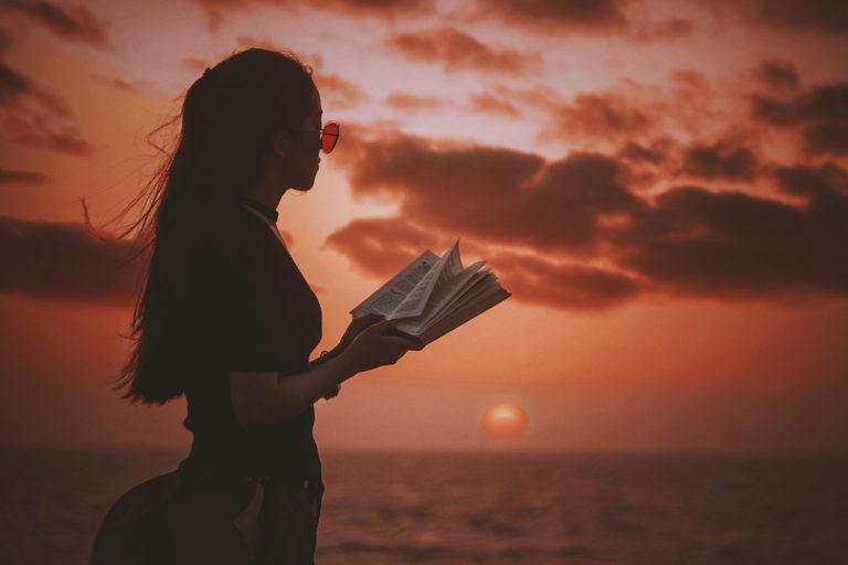 A woman reads a book at the beach at sunset