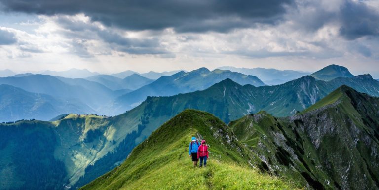 Two hikers make their way down a grassy ridge