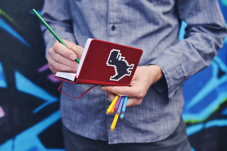 a man draws in a notebook decorated with a dinosaur sticker