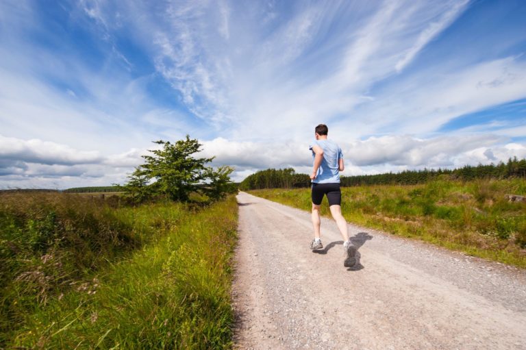 A man runs down a dirt trail on a beautiful sunny day