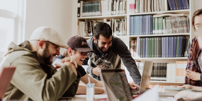a group of friends cluster around their laptops, laughing