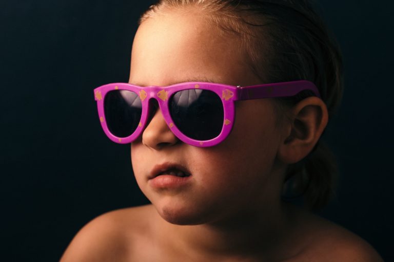 Young child in brightly colored sunglasses, pulling a face