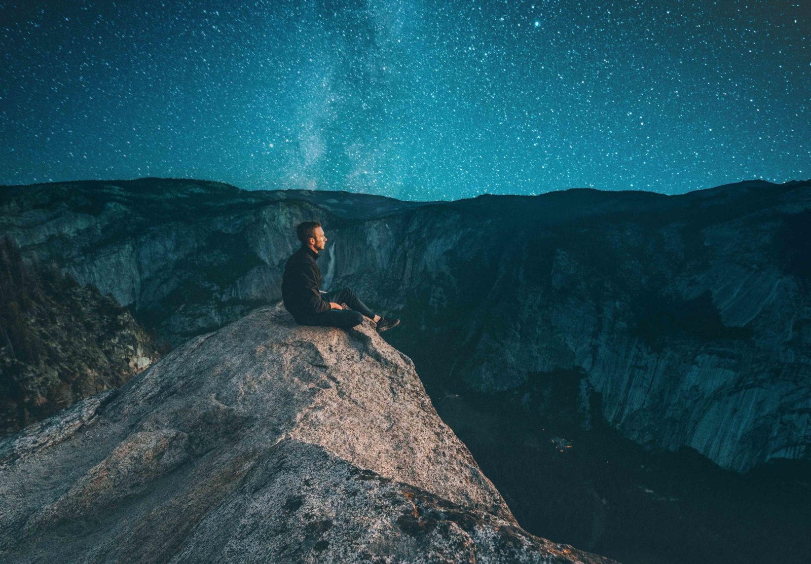 Man sitting on cliff looking at stars