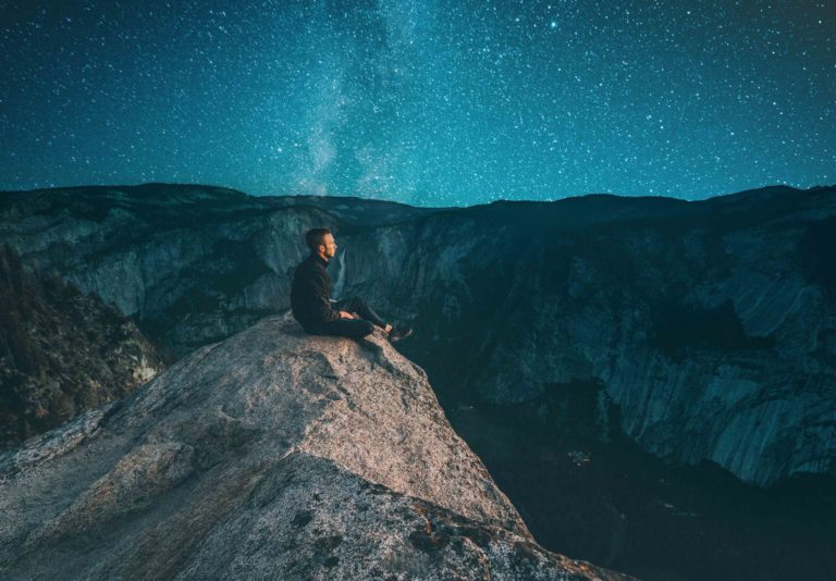 Man sitting on cliff looking at stars