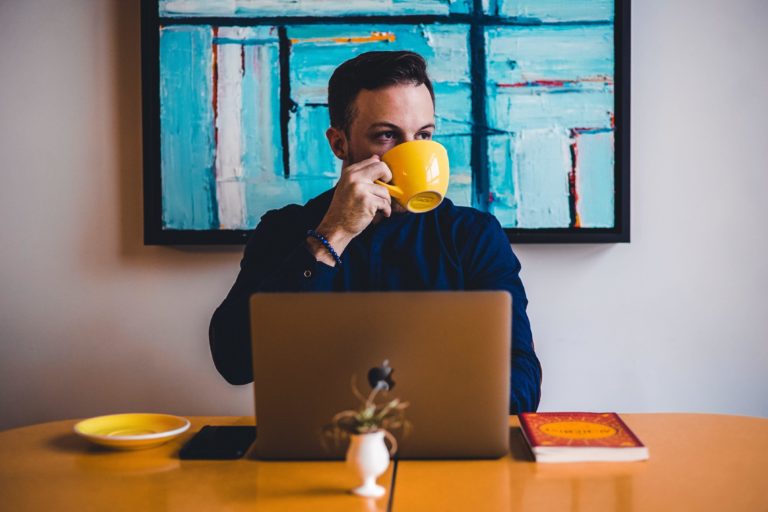 A man sips a cup of coffee at his computer.