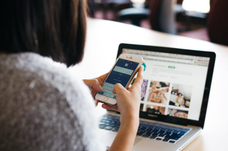 A woman checks her phone while also looking at her laptop.