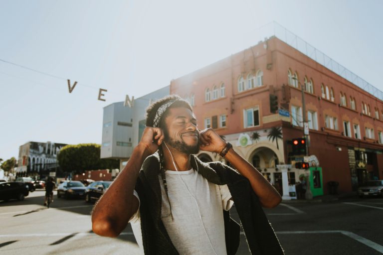 Man standing in the street listening to music with a smile on his face.