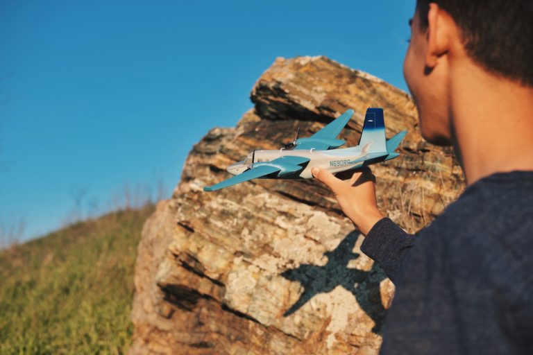 A man plays with a toy airplane under a blue sky.