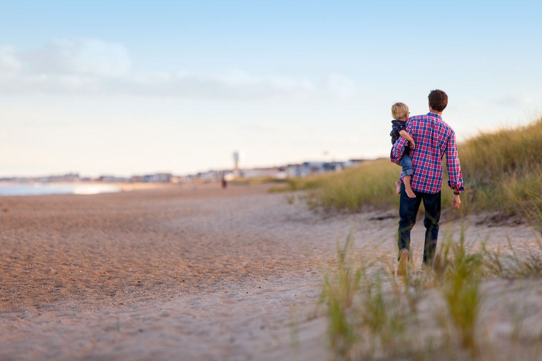 A father holds his child while gazing at a beach.