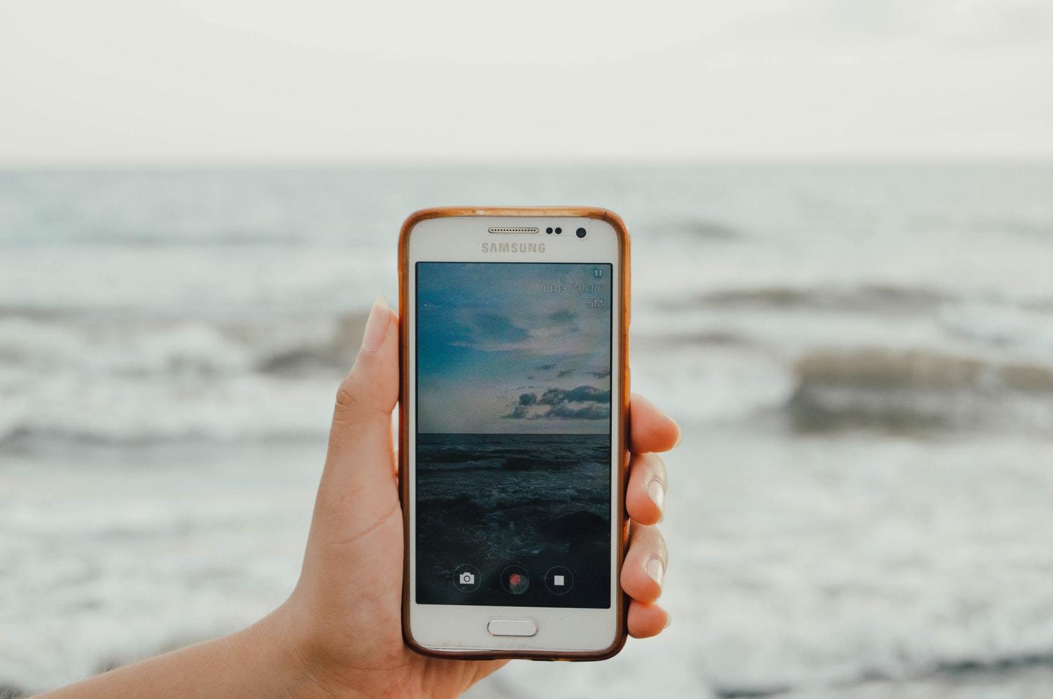 A person films a beach's waves with their iPhone.
