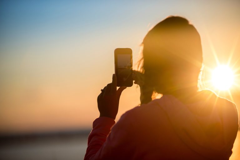 Woman taking photo of a sunset on a smartphone.