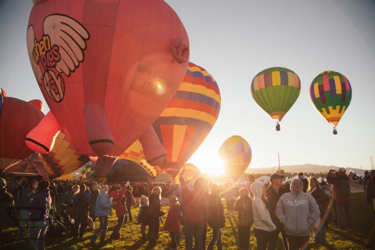A group of people gathers around a group of brightly colored hot air balloons.