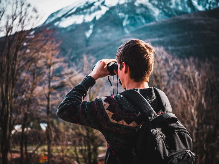 A man looks off into the wilderness with binoculars.