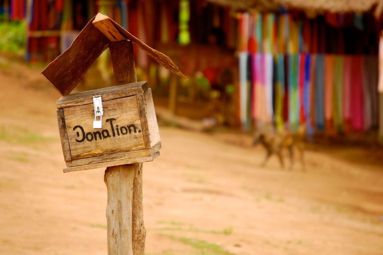 A wooden donation box on a sandy hill.