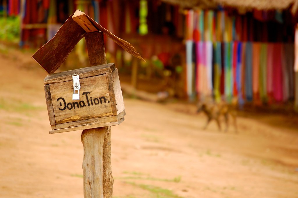 A wooden donation box on a sandy hill.