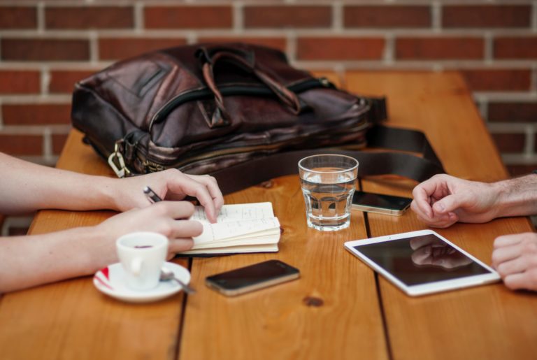 Two people meet at a coffee shop to discuss original research for marketing.