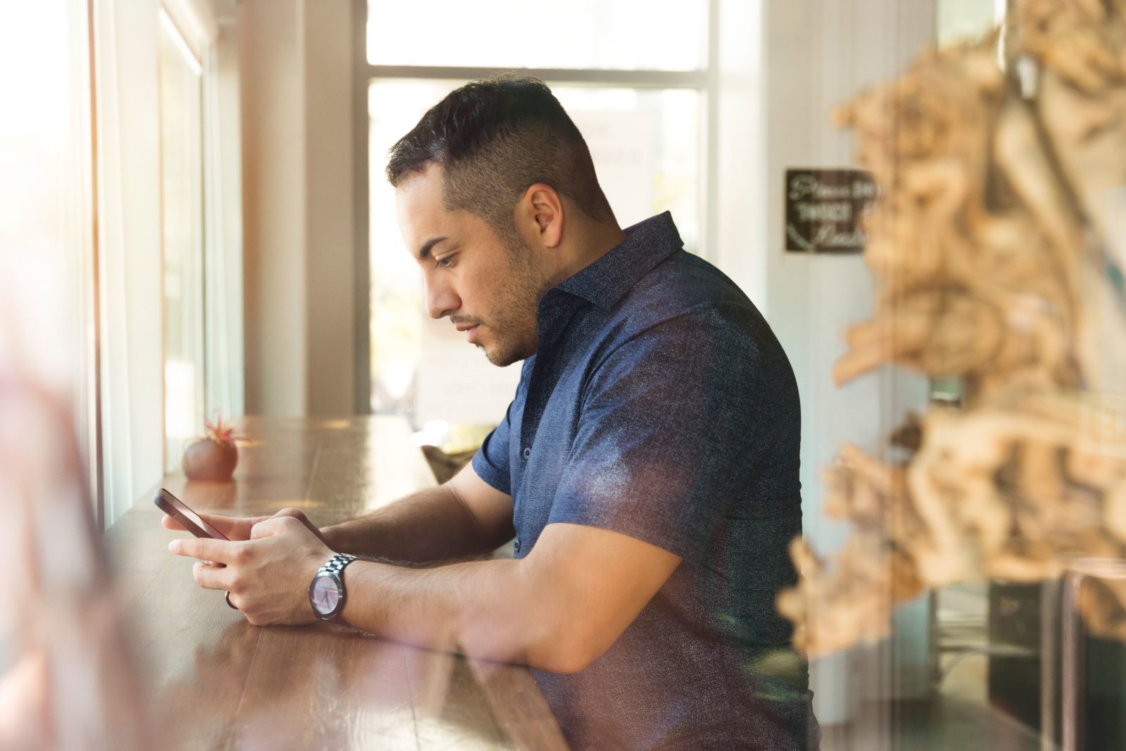 A man in a short-sleeved, button-up shirt reads an email marketing campaign in a cafe.