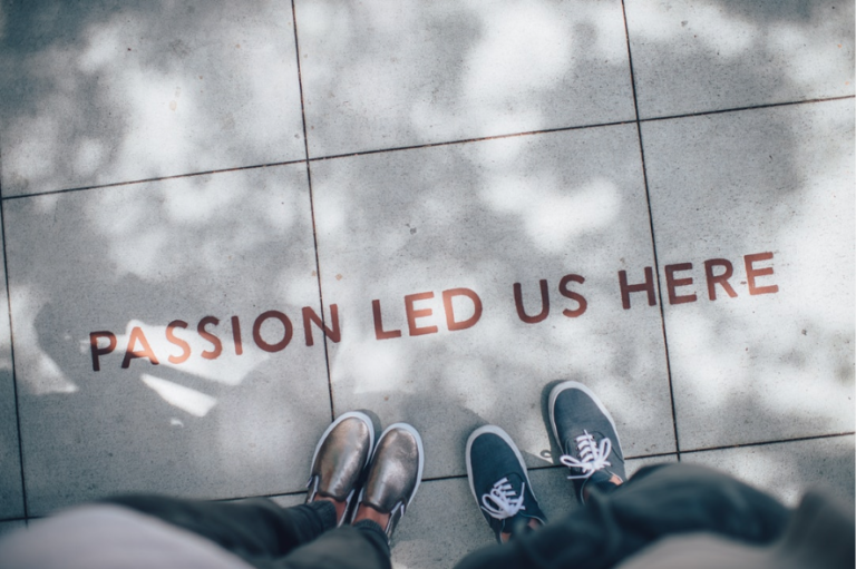 Two people stand in front of writing on a street that says "passion lead us here."