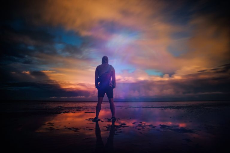 Man standing on beach looking at sunset.