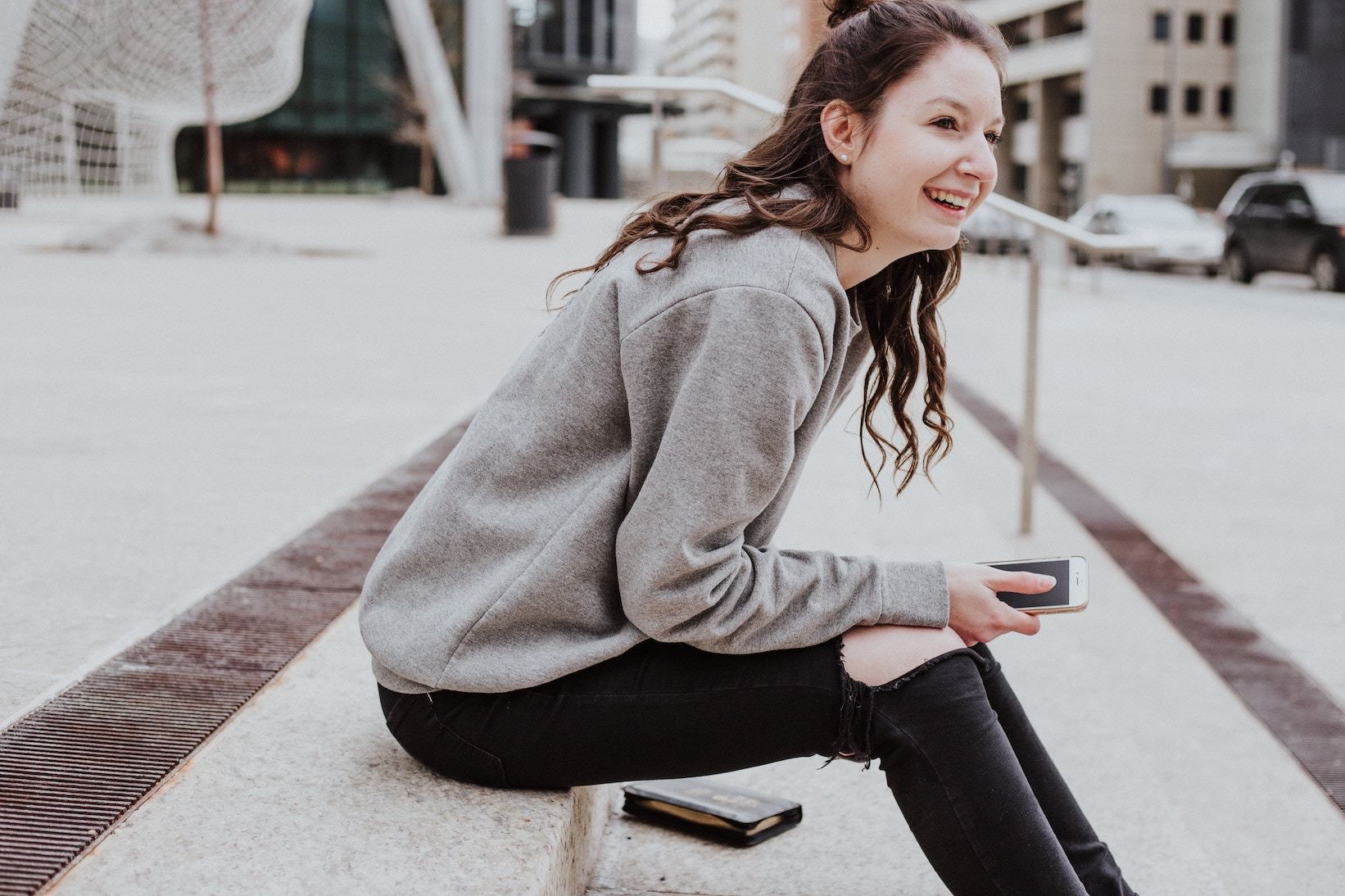 Woman sitting on step, holding smartphone and smiling