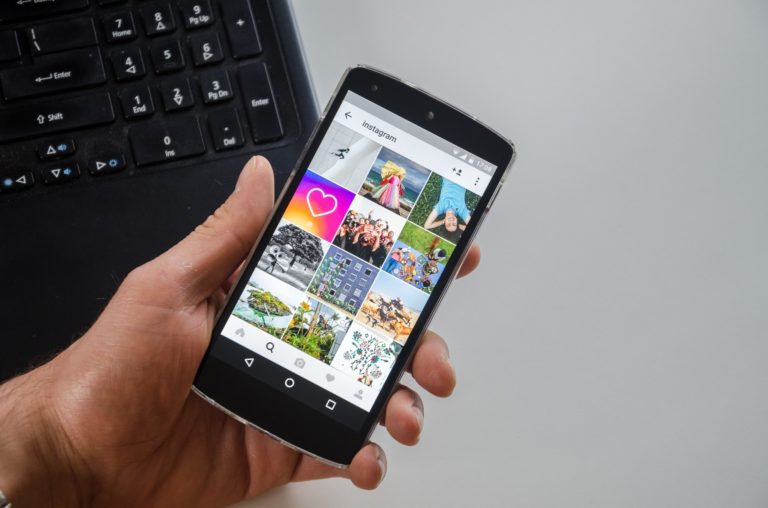 A person holding a phone with Instagram displayed over a laptop.