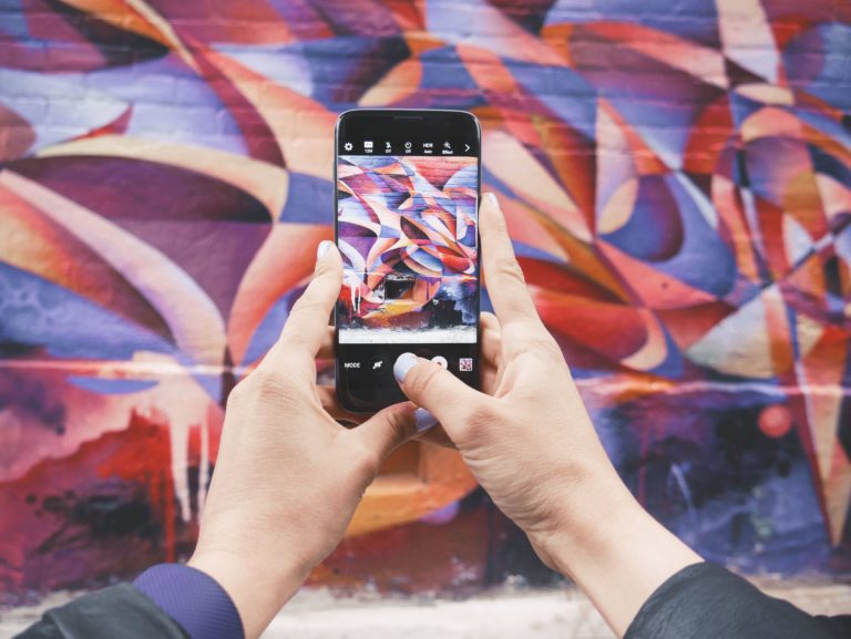 A person with purple painted nails takes a photo of geometric graffiti.