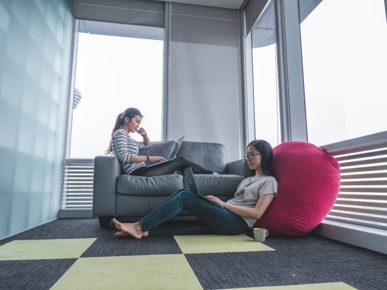 Two women work on SEO and PR outreach efforts while sitting on a couch.