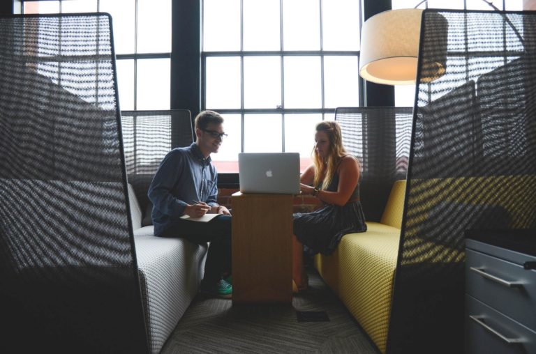 A male and a female from the C-suite meet to discuss business plans on a laptop.