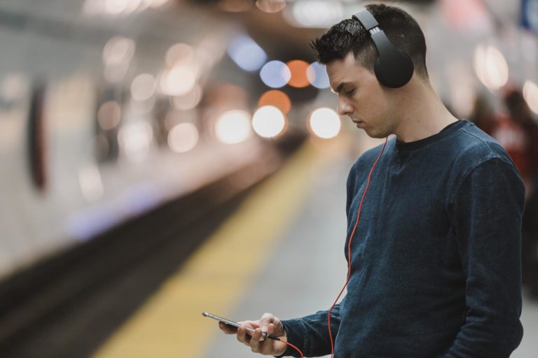 A young man listens to a podcast through over-ear headphones while waiting for his subway train to arrive.