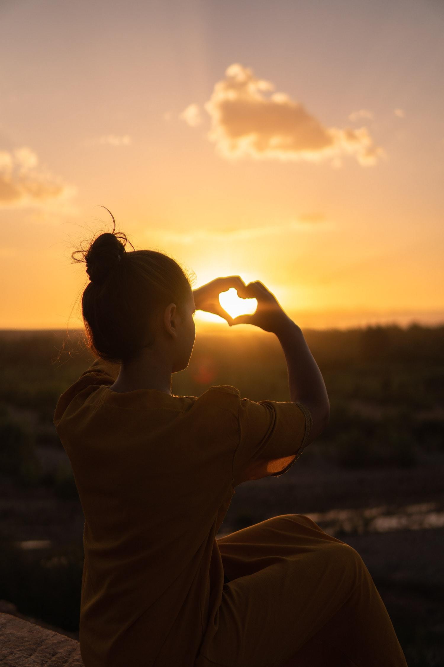Young woman forms the shape of a heart with her hands as the sun sets.
