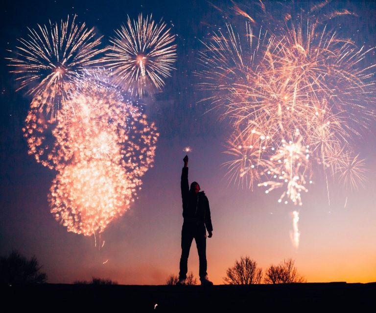 A content marketer holds up a sparkler as large fireworks light up the sky in the background.