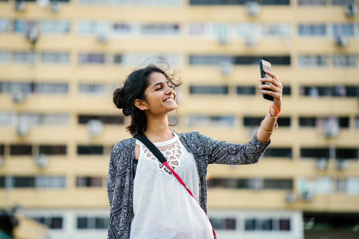 A smiling woman holds a smartphone in the air, gazing directly at it.