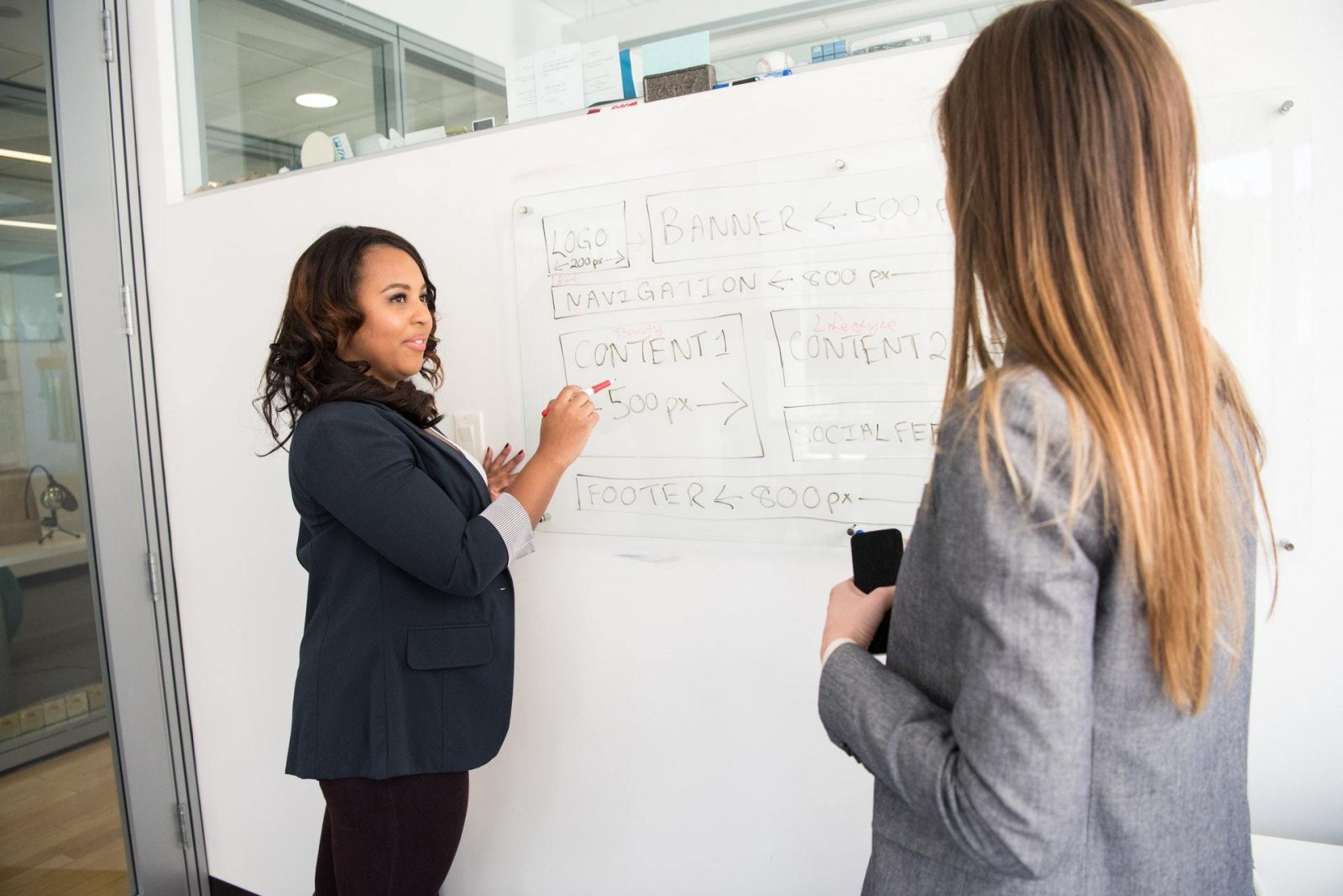 A female content marketing leader points to a content strategy on a whiteboard.