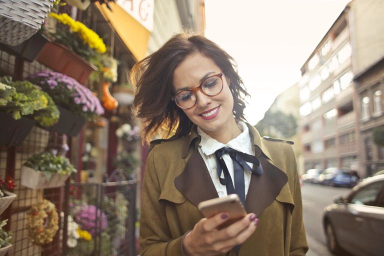 A woman wearing glasses uses voice search technology while walking on an empty street