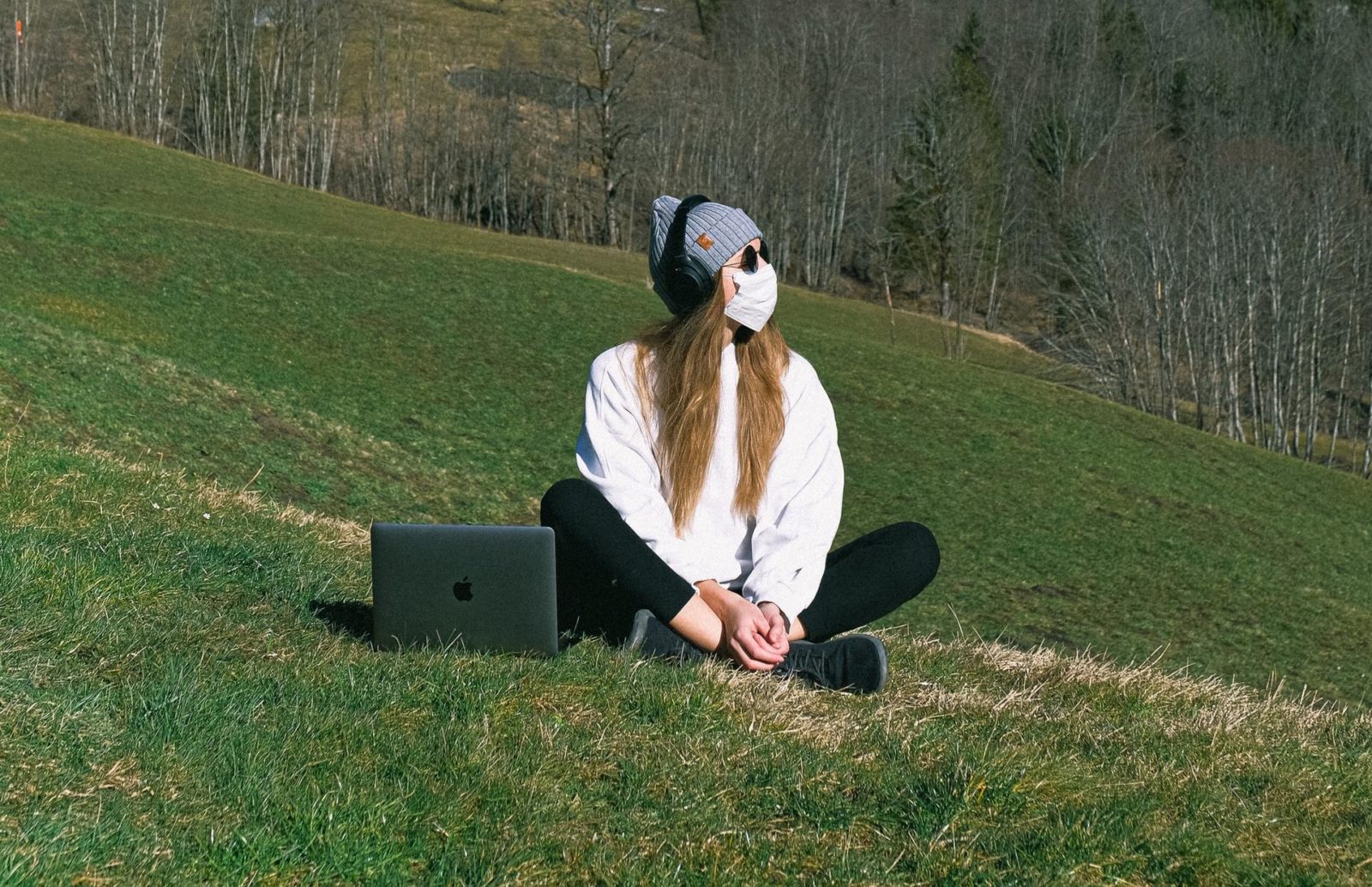 A woman on a marketing team sits on a patch of grass wearing a protective face mask