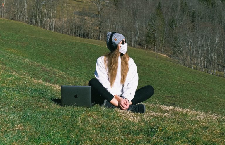 A woman on a marketing team sits on a patch of grass wearing a protective face mask
