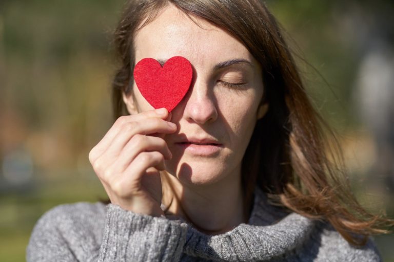 A woman holds a paper heart above her eye to symbolize empathetic marketing.