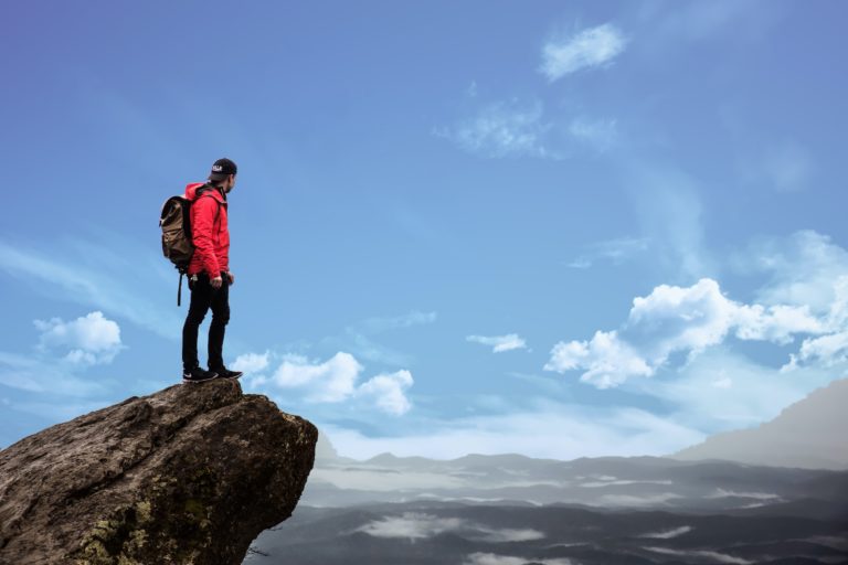 A man on top of a mountain looks out at a cloudy sky.
