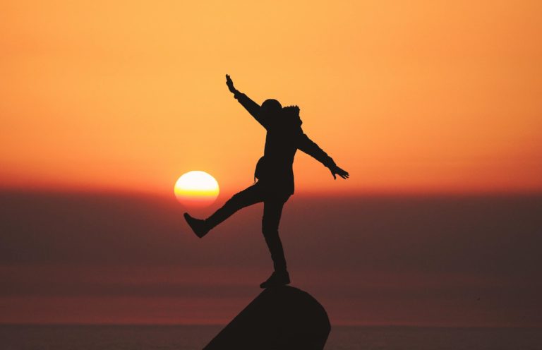 A man loses his balance on a rock while the sun sets behind him.