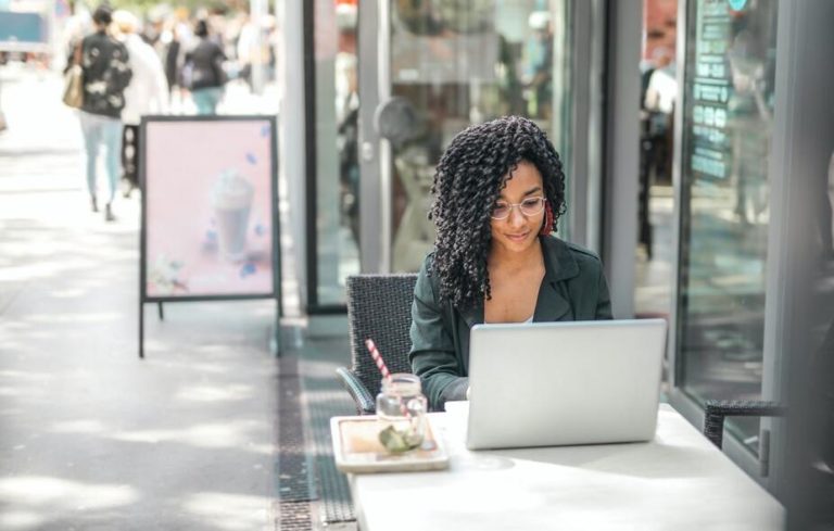 A freelance subject matter expert works on a content marketing article on her laptop while sitting outside at a cafe.