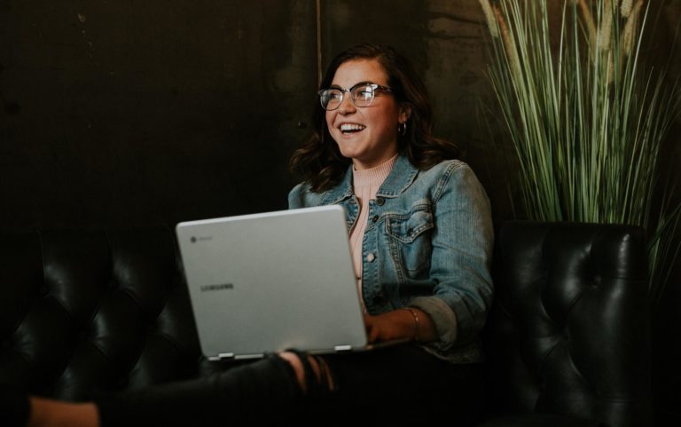 A woman sitting on a couch wearing glasses listens to a content marketing podcast.