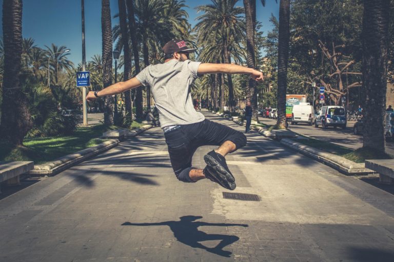 A man jumps and clicks his heels on street lined with palm trees.