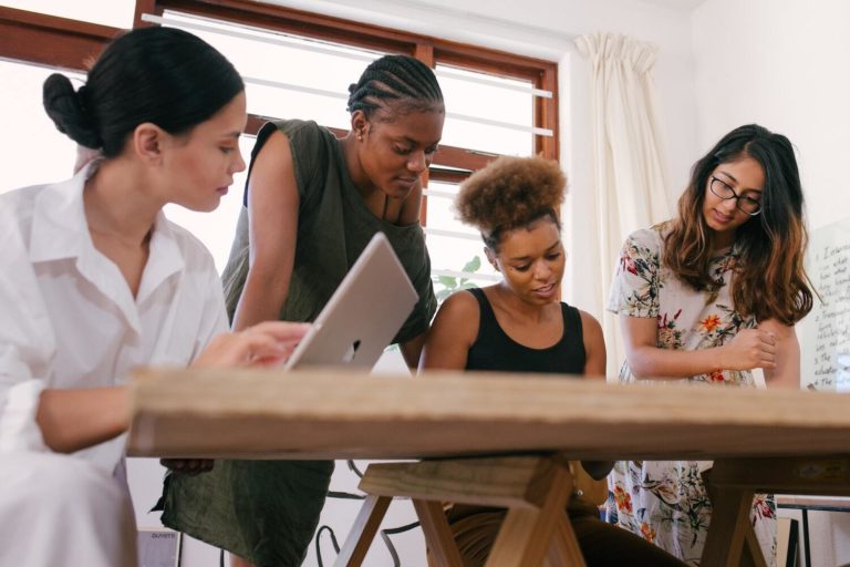 Four women gather around a table to discuss integrating content marketing competencies into their brand's strategy.