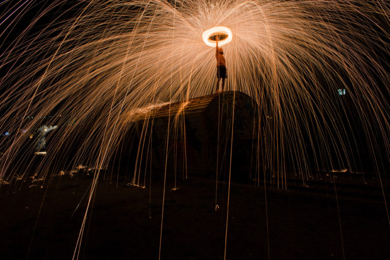 A person holds an illuminated halo while standing atop a tall structure.