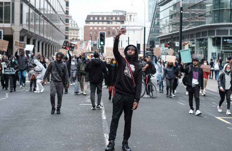 Man facing camera photographs the crowd behind him at a Black Lives Matter protest.