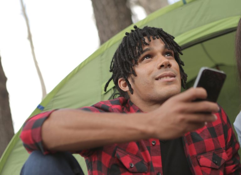 Man camping in the woods uses voice search via Siri on a smartphone.