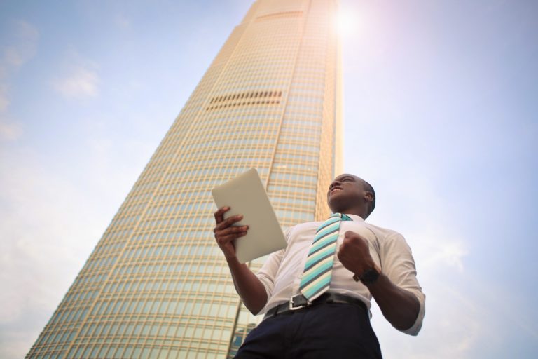 Man holding tablet, standing in front of skyscraper